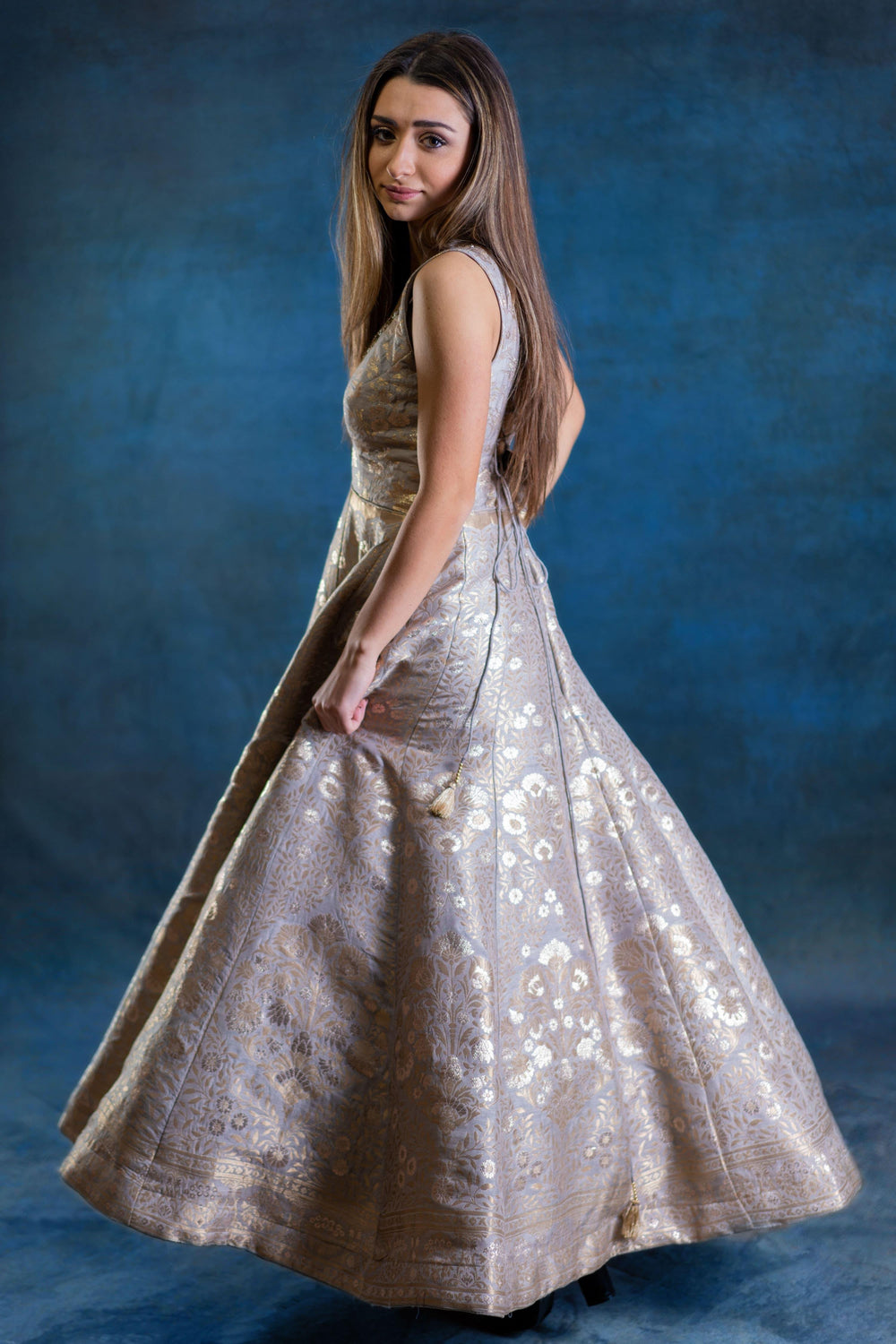 Woman in a gold jacquard silk A-line gown with intricate woven patterns and a sleeveless design.