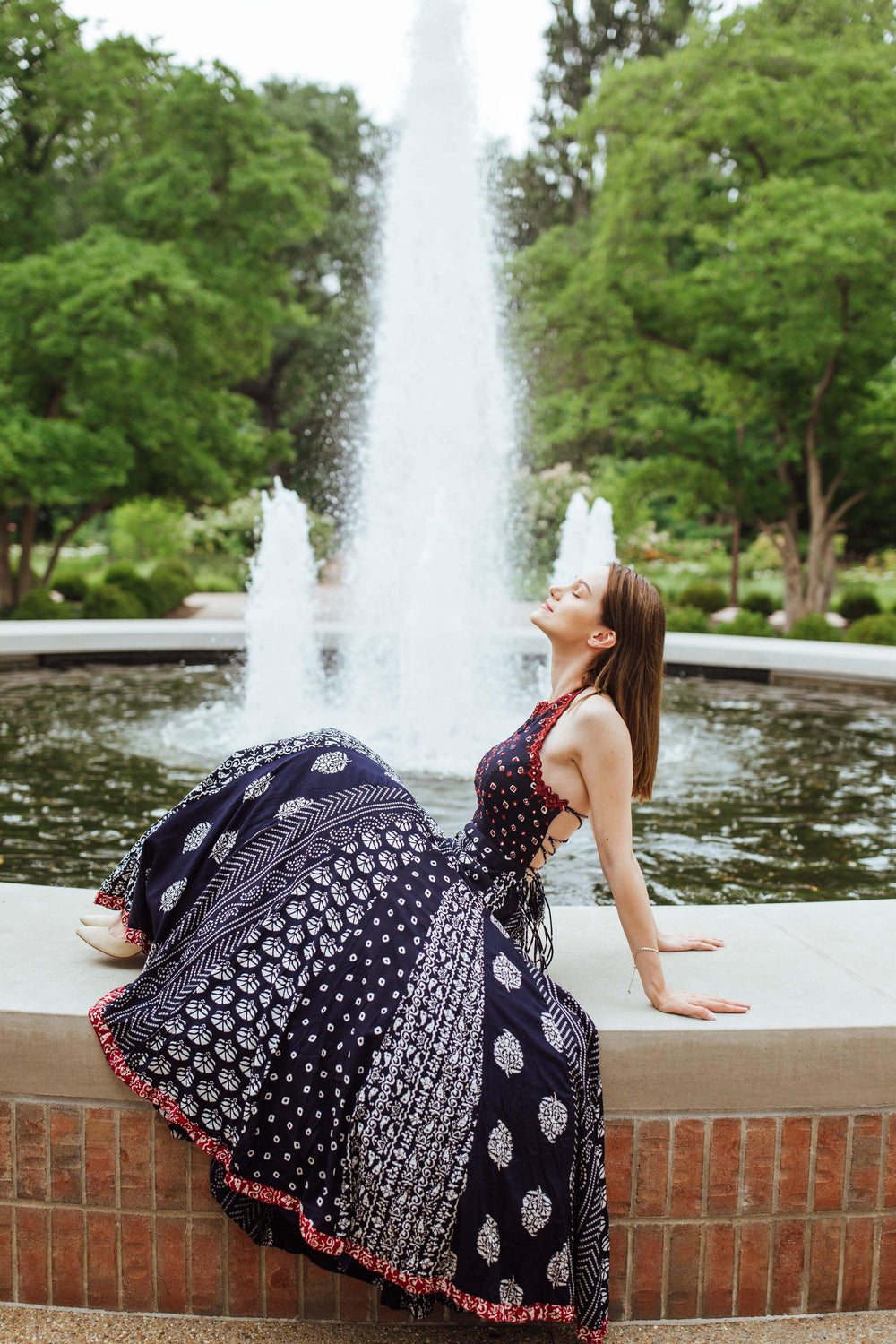 Woman in a navy and white printed cotton gown with red trim, sitting by a fountain.