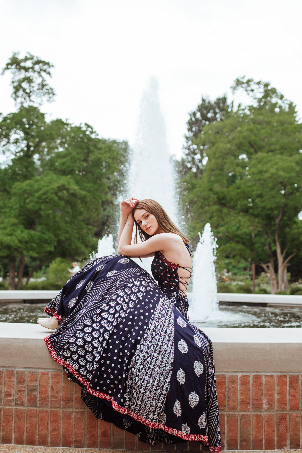 Woman in a dark blue printed maxi dress with a tie-back bodice, sitting by a fountain.