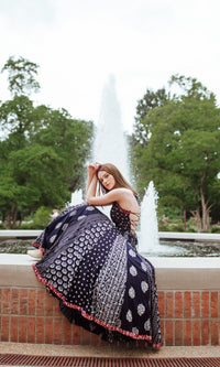 Woman in a dark blue printed maxi dress with a tie-back bodice, sitting by a fountain.