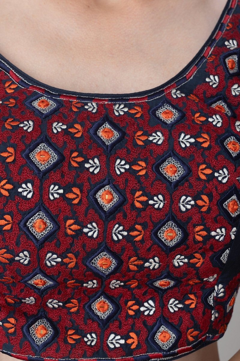Close-up of a red silk blouse with intricate orange, white, and navy embroidery, perfect for Garba.