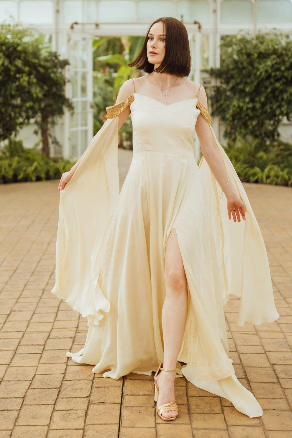 Beige silk long dress with shoulder capes and a high slit, worn by a model.