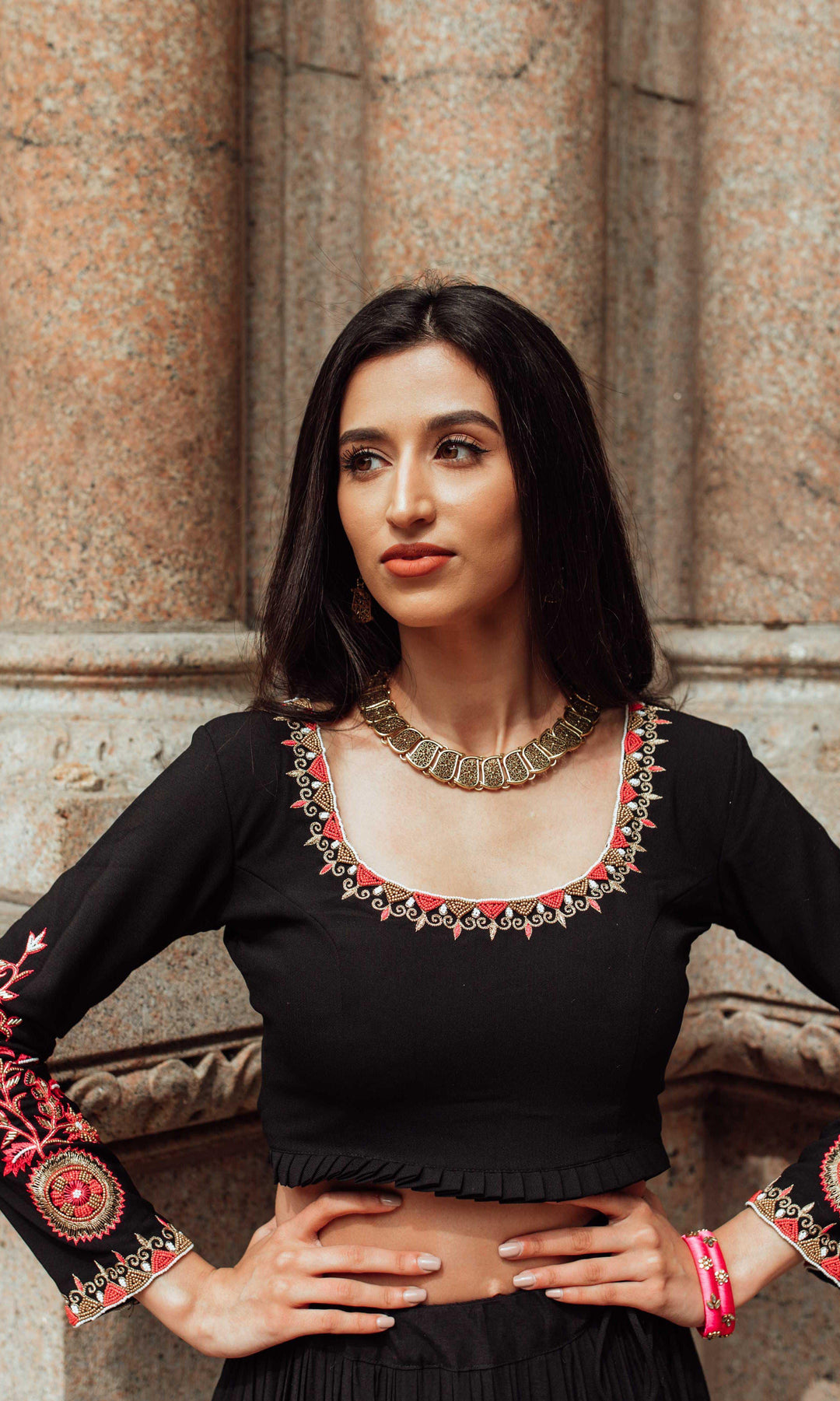 Woman in black silk chaniya choli with gold butta, intricate pearl, bead, and thread embroidery, and gold necklace.