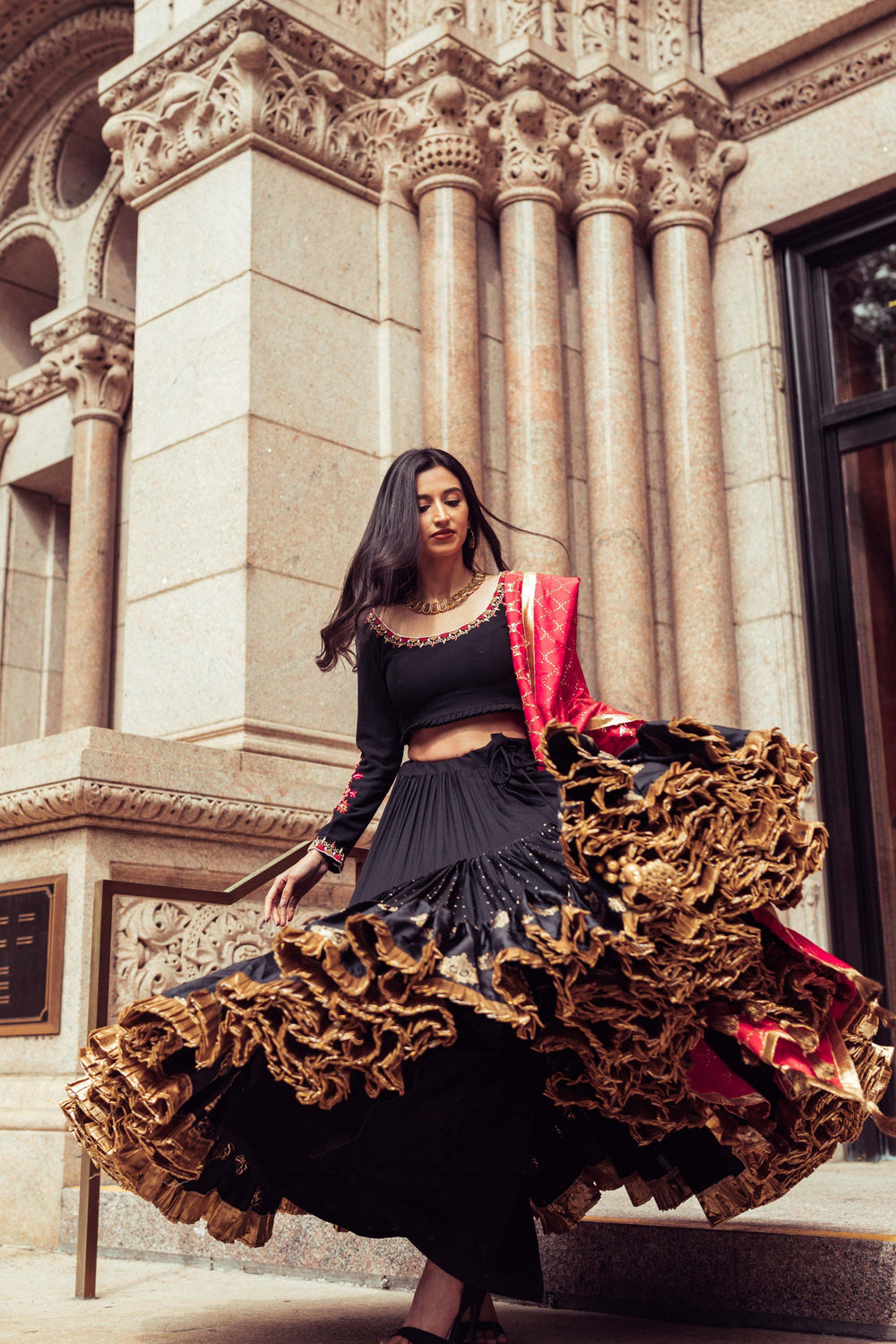 Woman in a black silk full flare Chaniya Choli with gold butta, pearl embroidery, and a red dupatta, dramatically twirling.