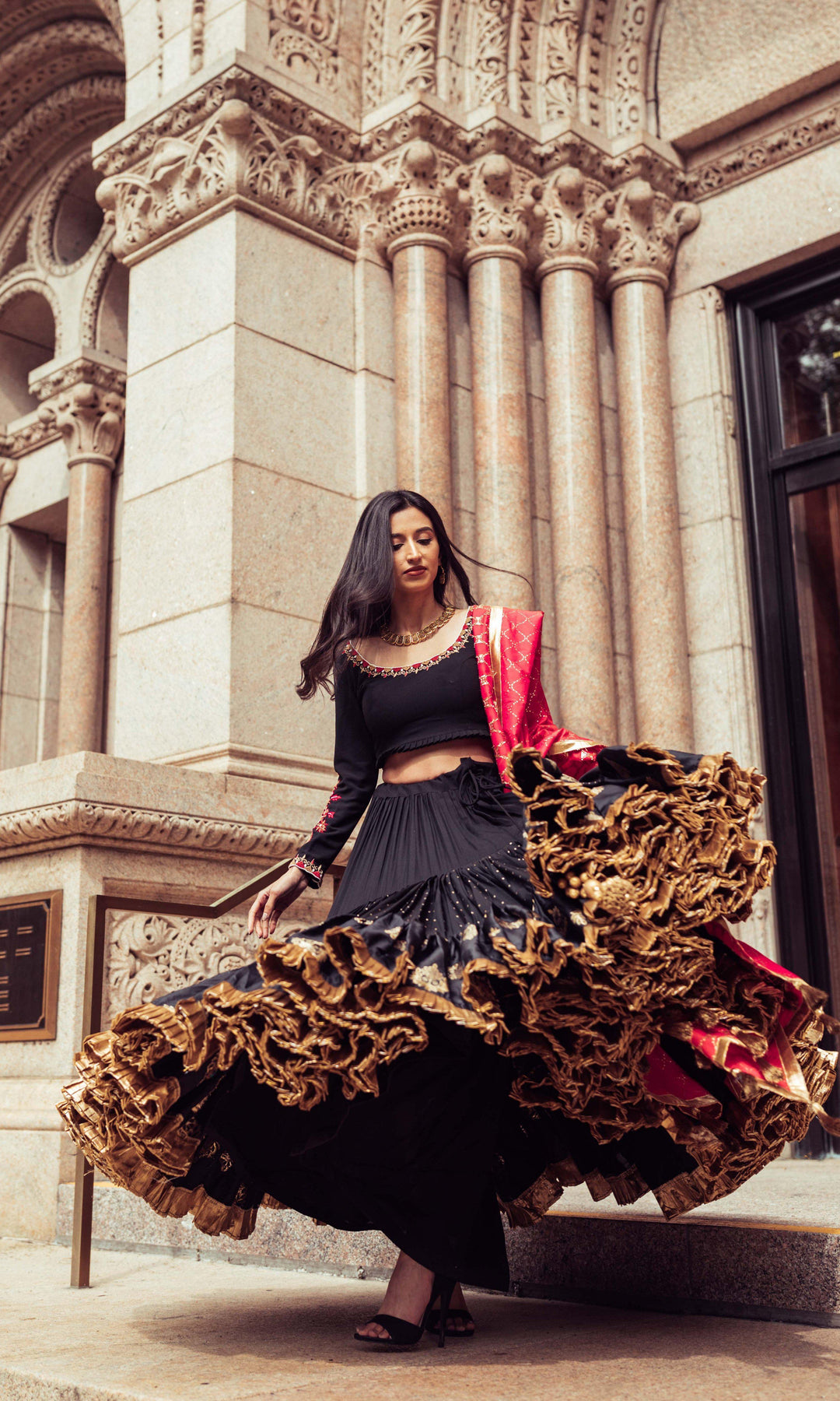 Woman in a black silk full flare Chaniya Choli with gold butta, pearl embroidery, and a red dupatta, dramatically twirling.