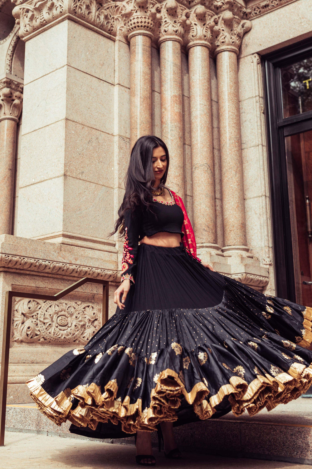 Woman in a black silk full flare chaniya choli with gold butta motifs, twirling dramatically.