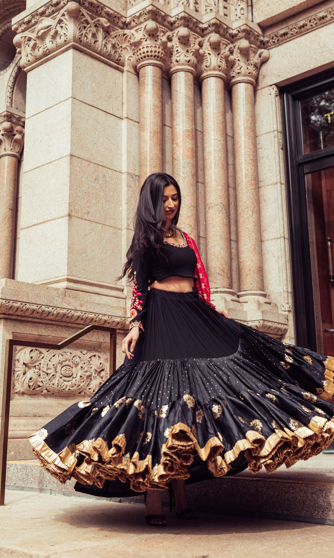 Woman in a black silk full flare chaniya choli with gold butta motifs, twirling dramatically.