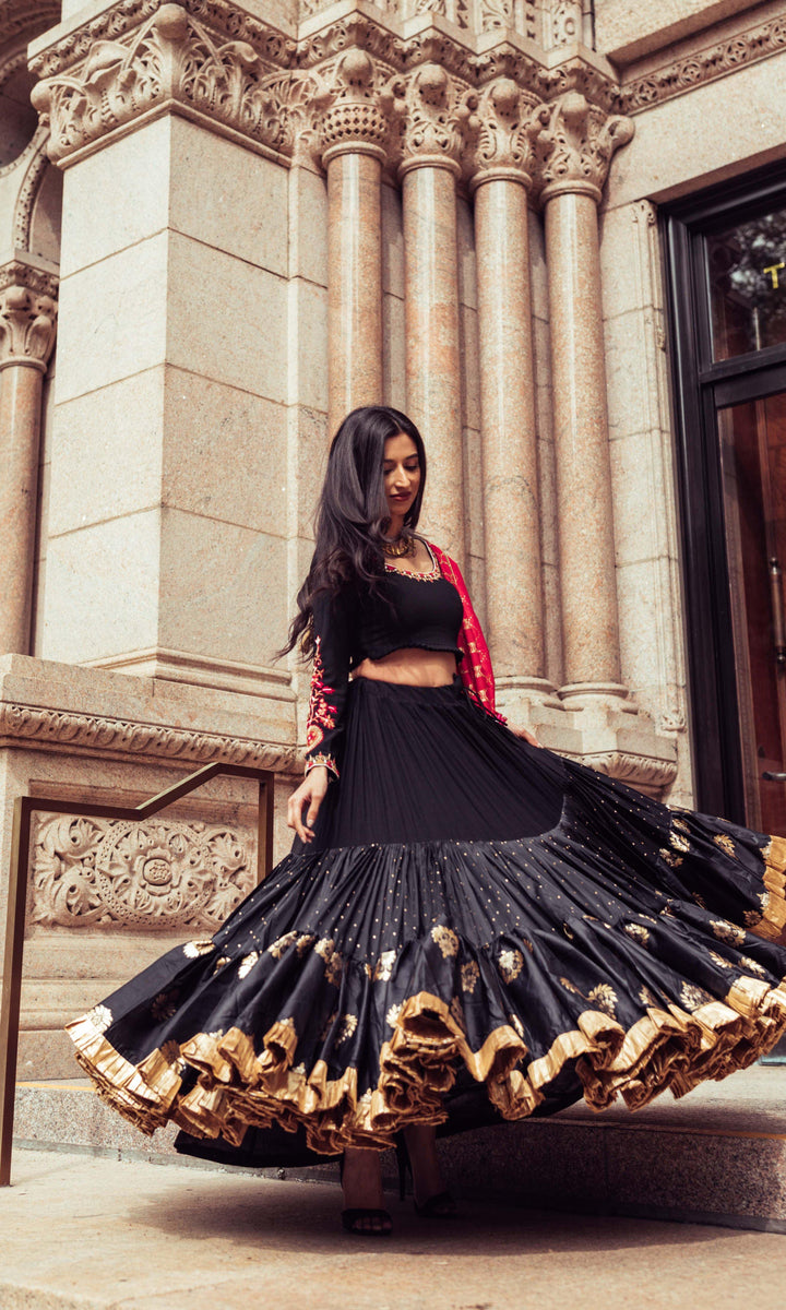 Woman in a black silk full flare chaniya choli with gold butta motifs, twirling dramatically.