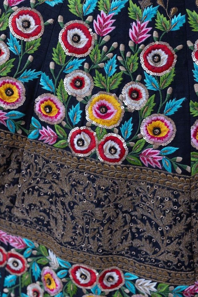 Close-up of a black gown with vibrant floral hand-embroidery and a gold-bordered net drape.