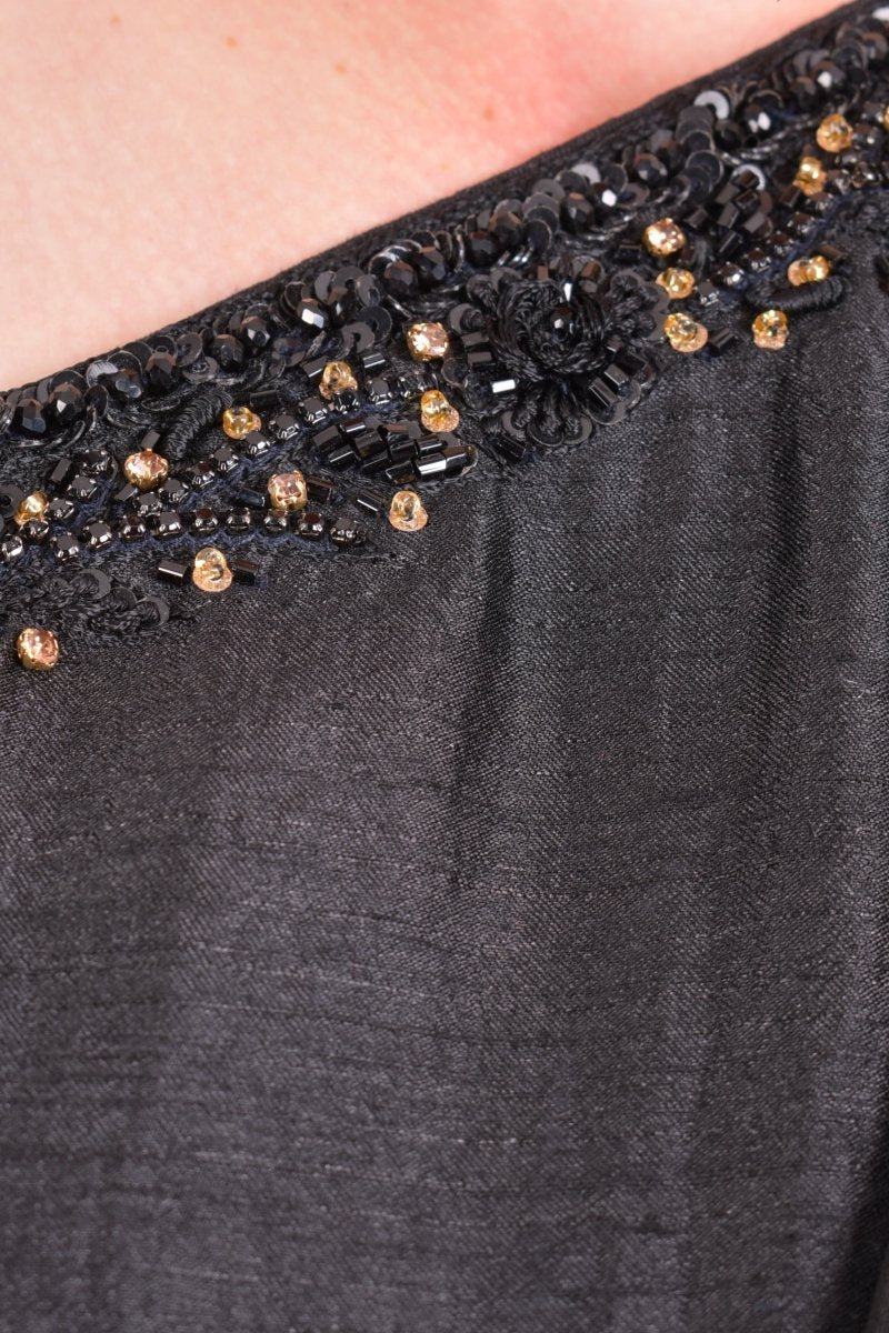 Close-up of black raw silk one-shoulder saree gown with intricate gold and black sequin, stone, and crystal embroidery.