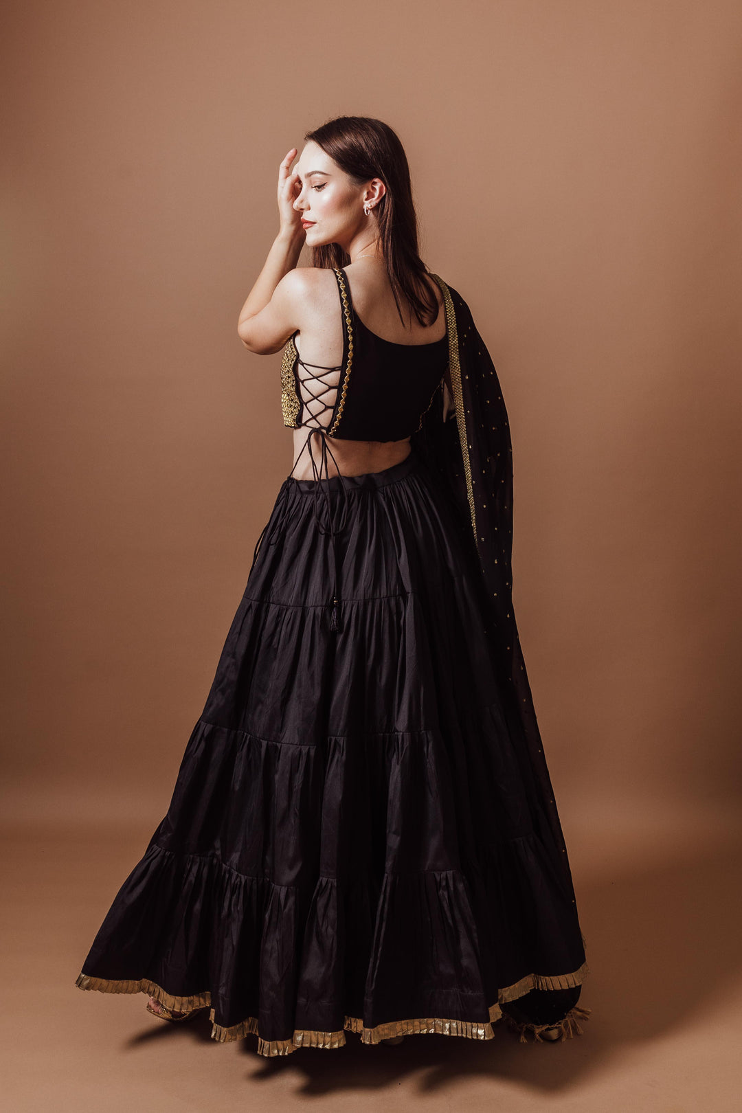 Woman in a black and gold lehenga set, sleeveless blouse with mirror work, and a flowing georgette dupatta.