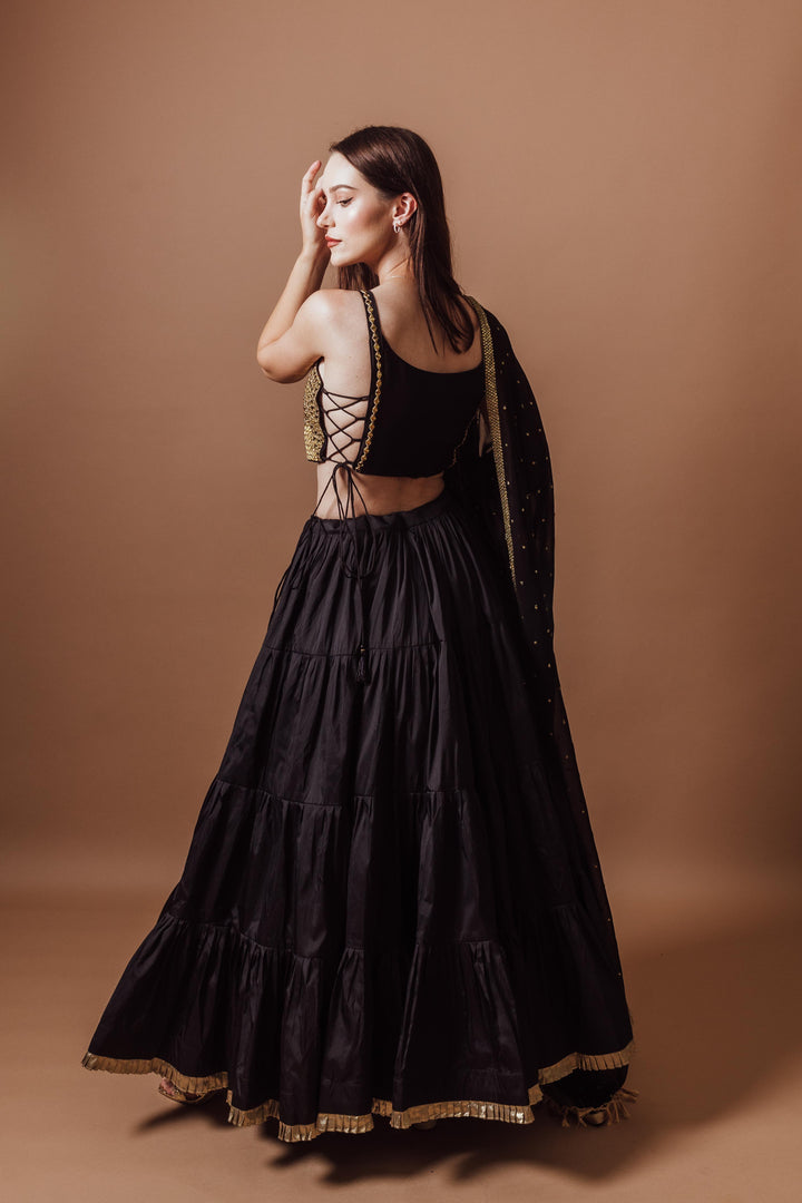 Woman in a black and gold lehenga set, sleeveless blouse with mirror work, and a flowing georgette dupatta.