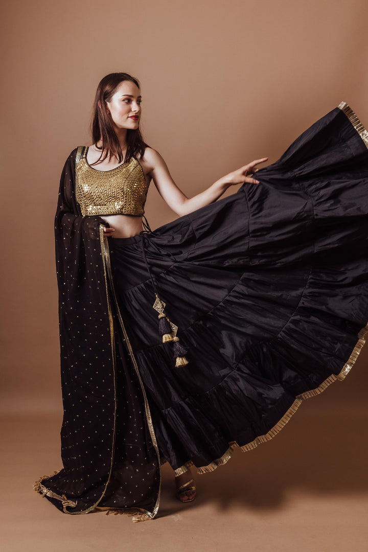 Victoria Black and Gold Lehenga Set: woman in sleeveless, mirror-embroidered blouse and flowing black silk lehenga.