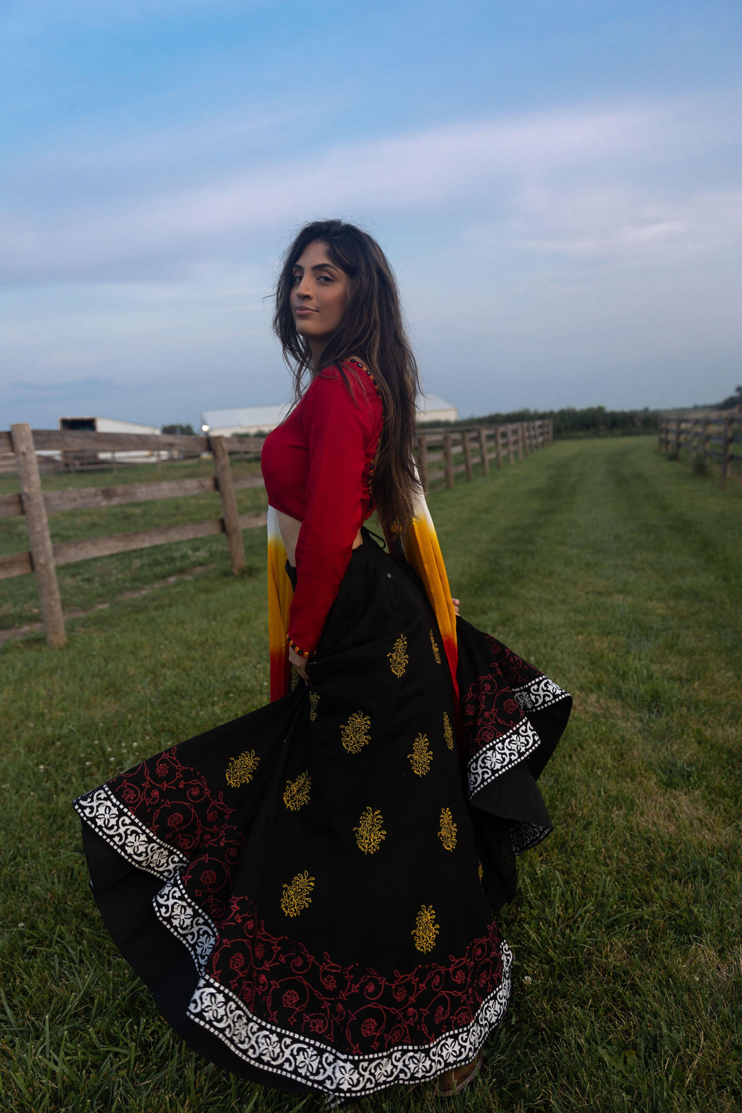 Woman in a dramatic twirl wearing a black cotton lehenga with yellow-gold and red print, red long-sleeve blouse, and shaded dupatta.