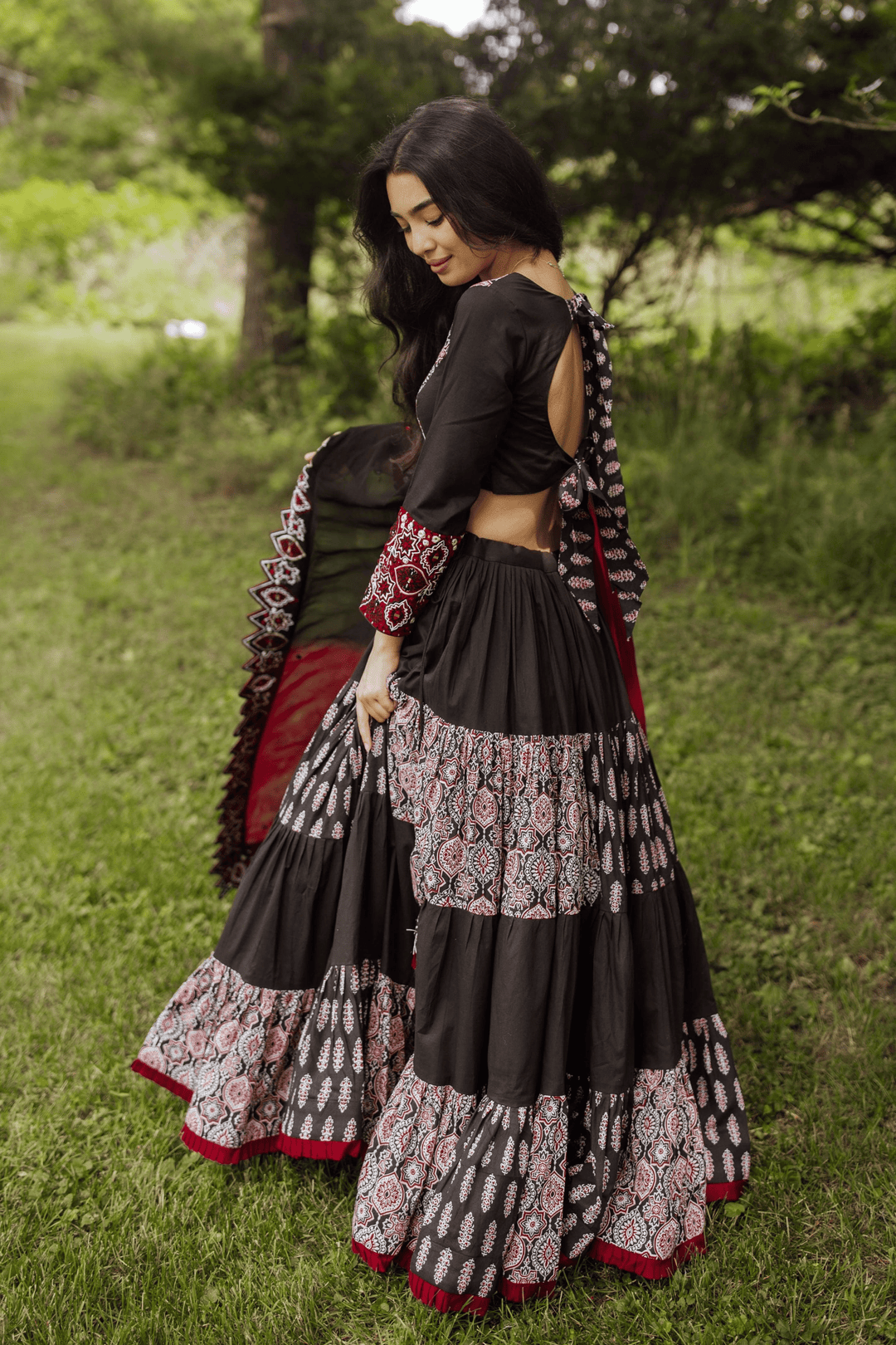 Woman in a black and red flared tiered silk lehenga choli set, twirling outdoors.