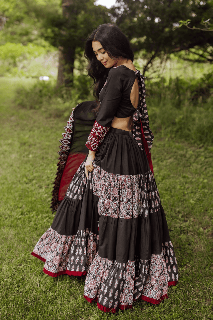Woman in a black and red flared tiered silk lehenga choli set, twirling outdoors.