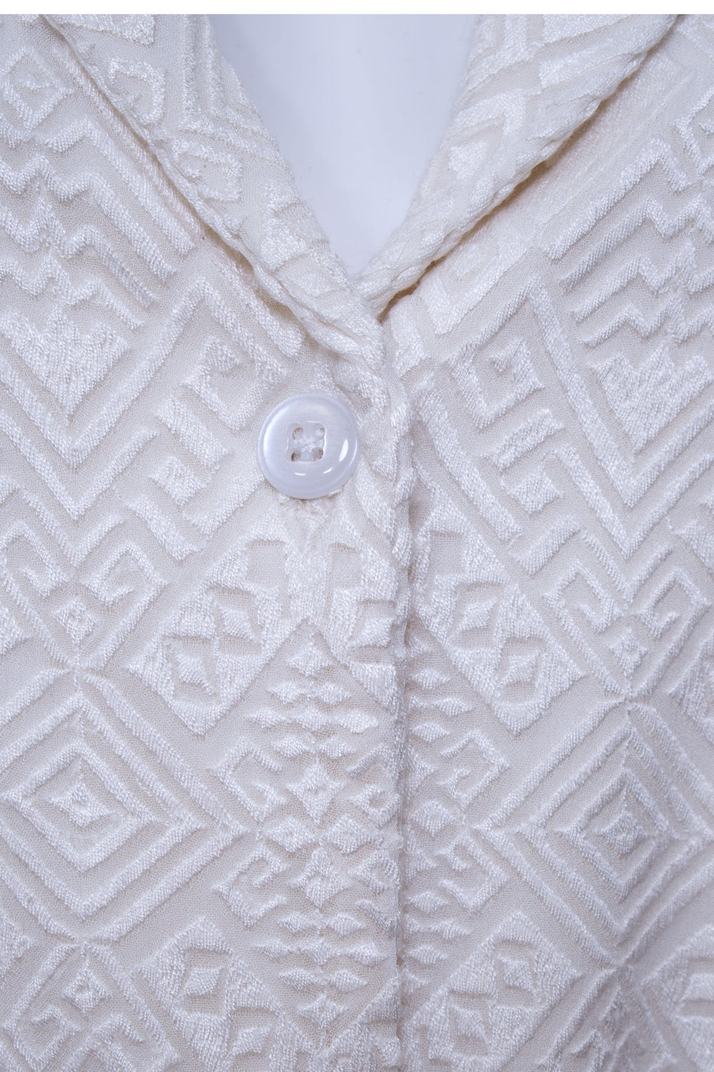 Close-up of a white georgette blazer dress with all-over self-thread geometric embroidery and a single button closure.