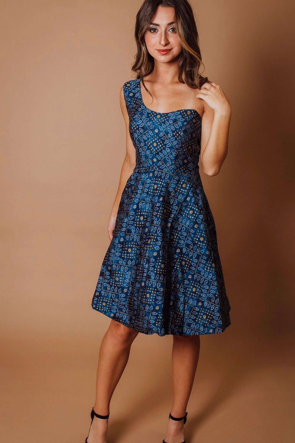 Blue silk one-shoulder midi dress with all-over bandhani print, worn by a woman.