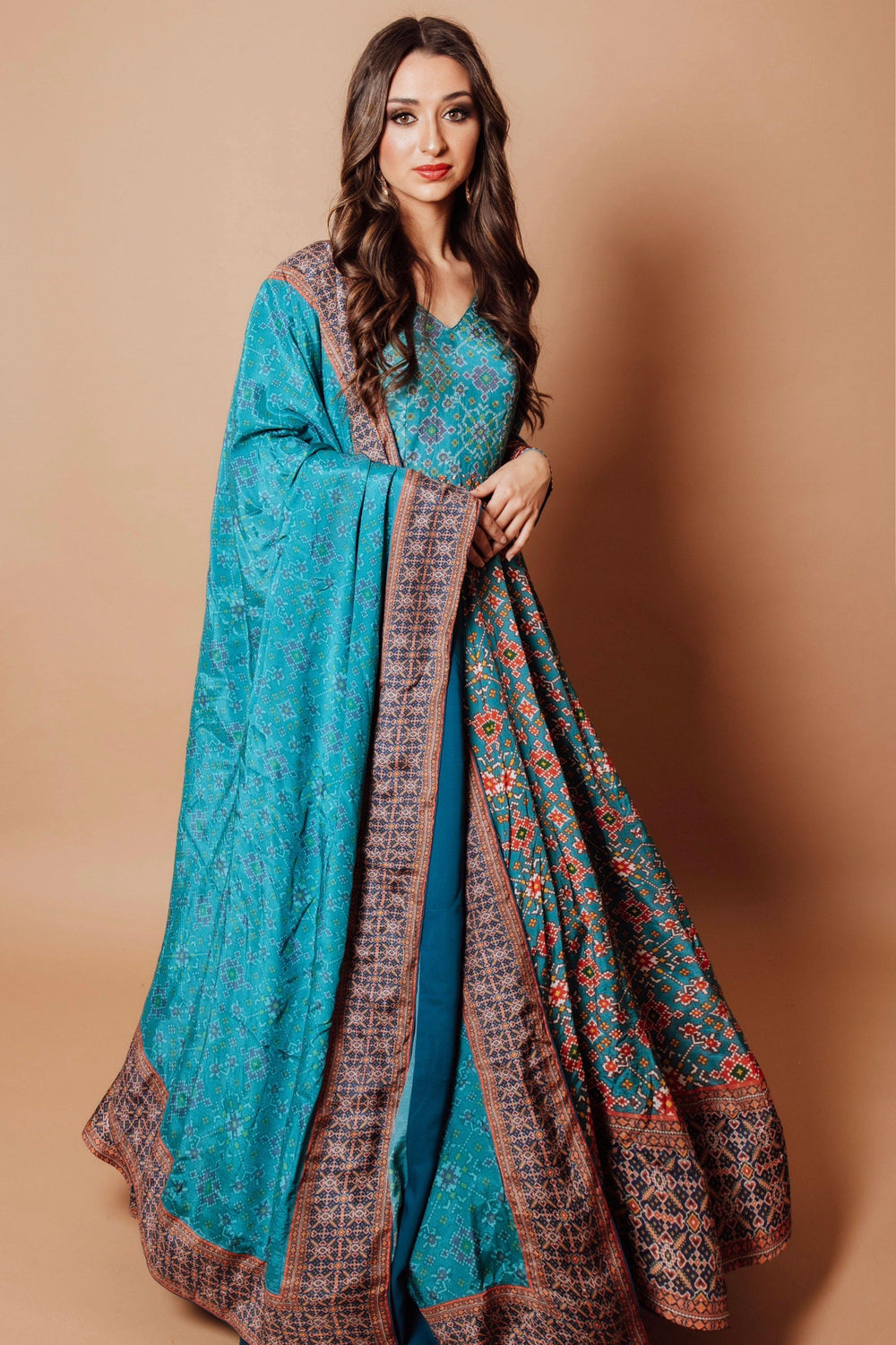 Blue patola print silk gown with integrated drape, featuring intricate resham embroidery and long sleeves.
