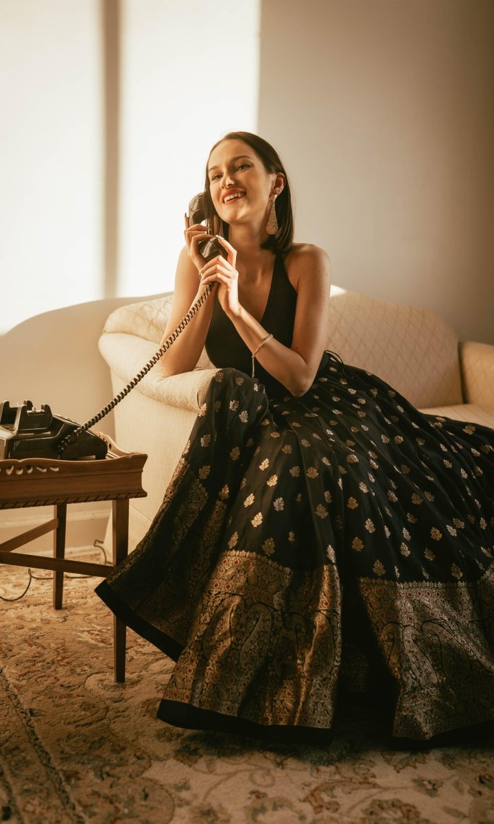 Woman in a blue silk gown with a gold Banarasi border, V-neck, and open back, holding a vintage phone.
