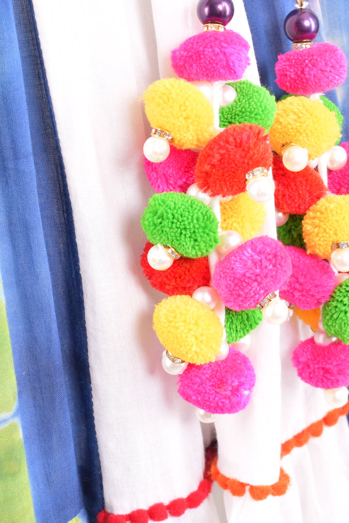 Close-up of vibrant pom-pom and pearl embellishments on a white cotton chaniya choli with blue tie-dye.