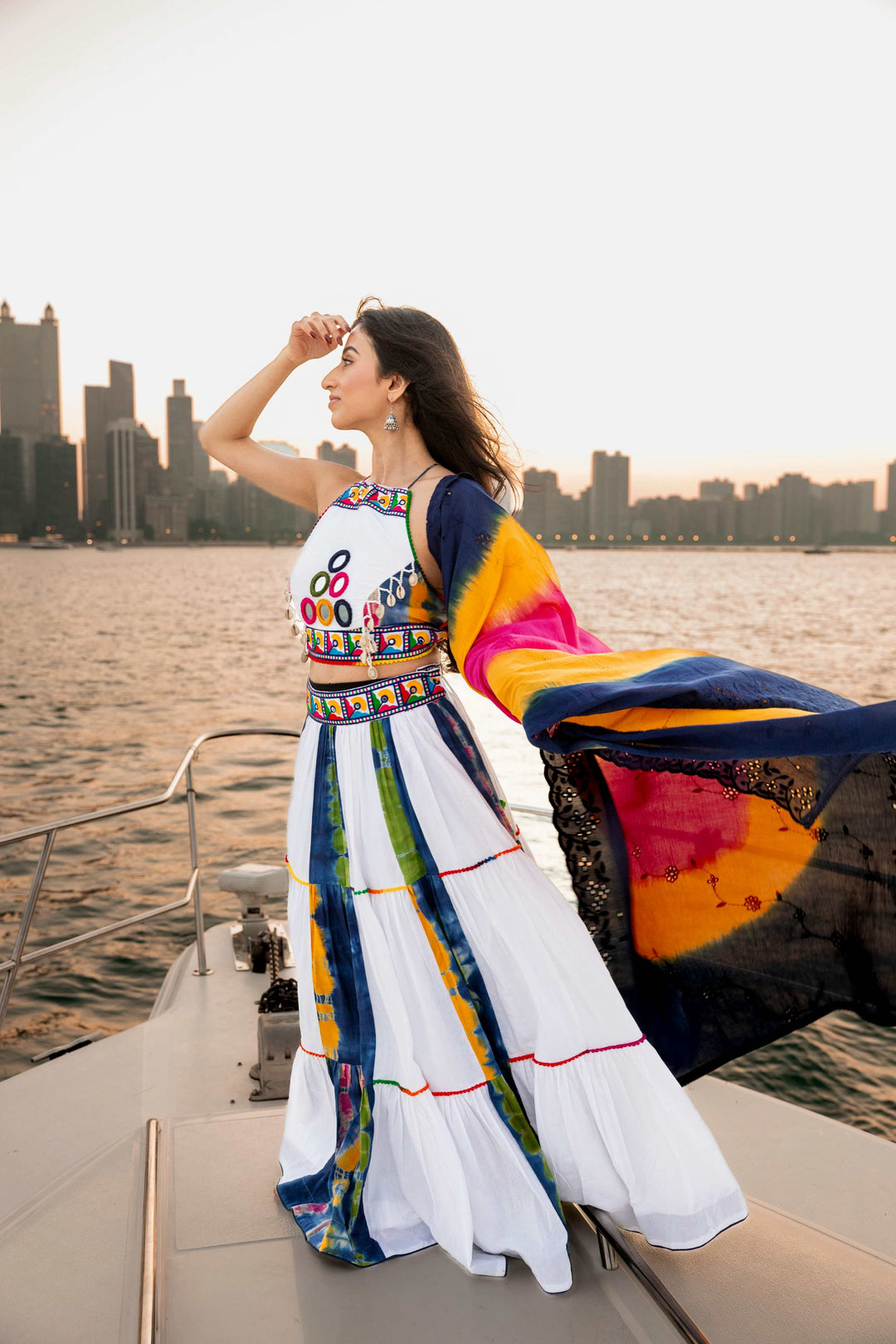 Woman in white cotton tie-dye Chaniya Choli with mirror-work blouse, dupatta flowing, on a boat.