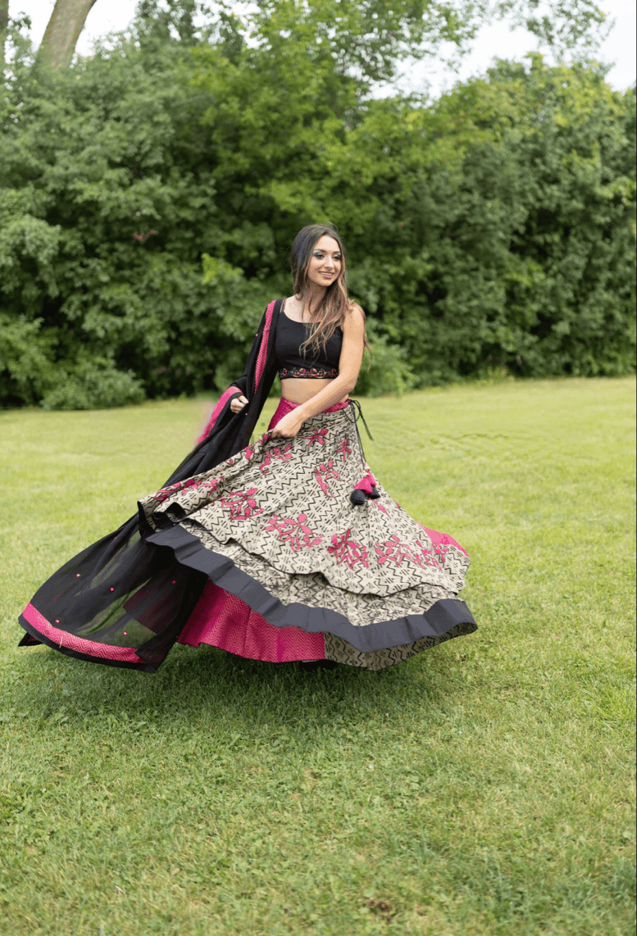Woman in embroidered multicolor cotton-silk Chaniya Choli set, black blouse, and dupatta, dramatically twirling in grass.