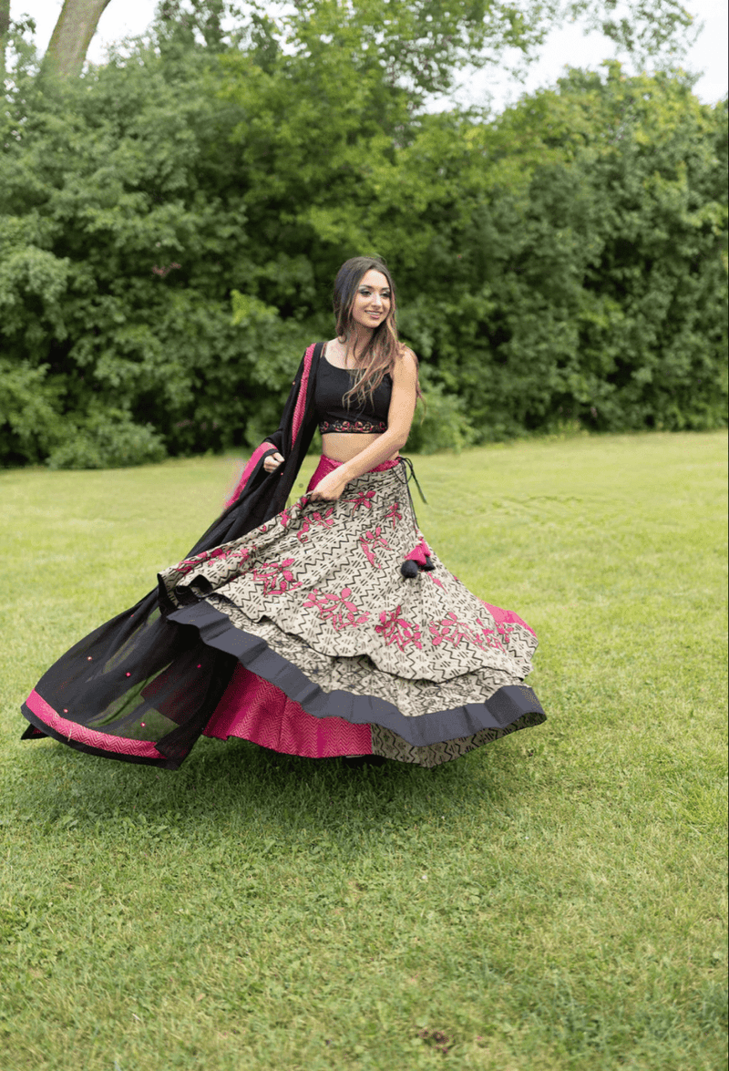 Woman in embroidered multicolor cotton-silk Chaniya Choli set, black blouse, and dupatta, dramatically twirling in grass.