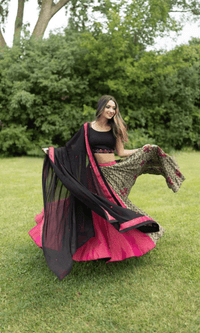 Woman in embroidered multicolor cotton-silk Chaniya Choli set, black blouse, fuchsia skirt, and black dupatta, twirling outdoors.