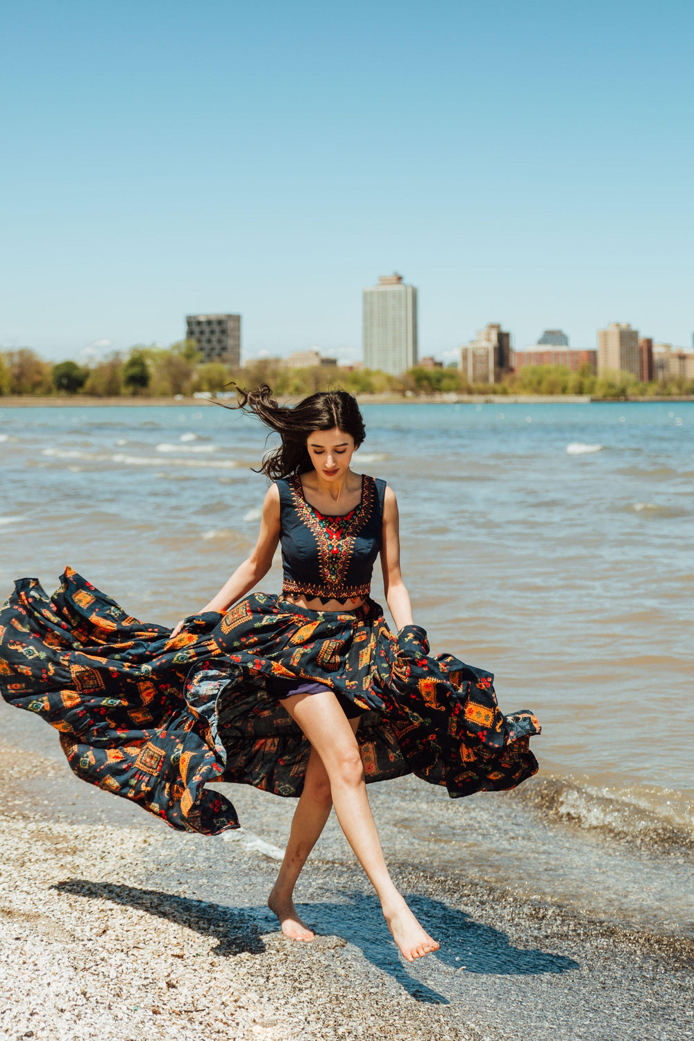 Embroidered navy high-low skirt set with a crop top and a flowing, printed skirt on a beach.