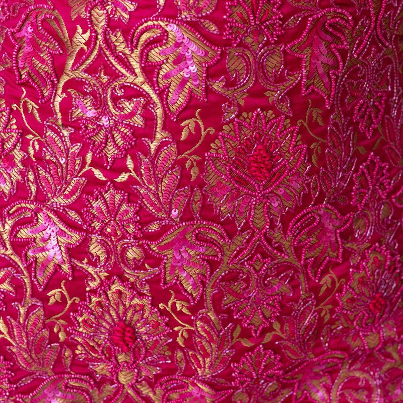 Close-up of fuchsia pink banarasi silk fabric with intricate gold and pink sequin floral embroidery.