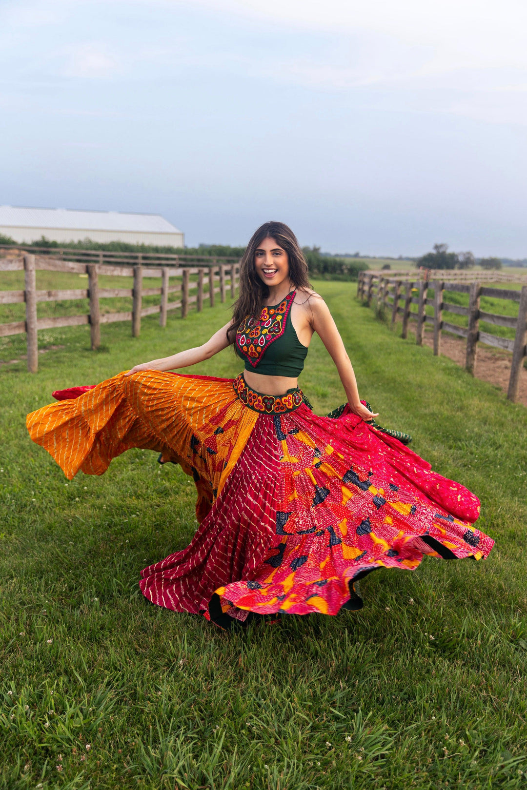 Woman in a full flare multicolor Chaniya Choli, green embroidered top, and dramatic twirl skirt in a field.