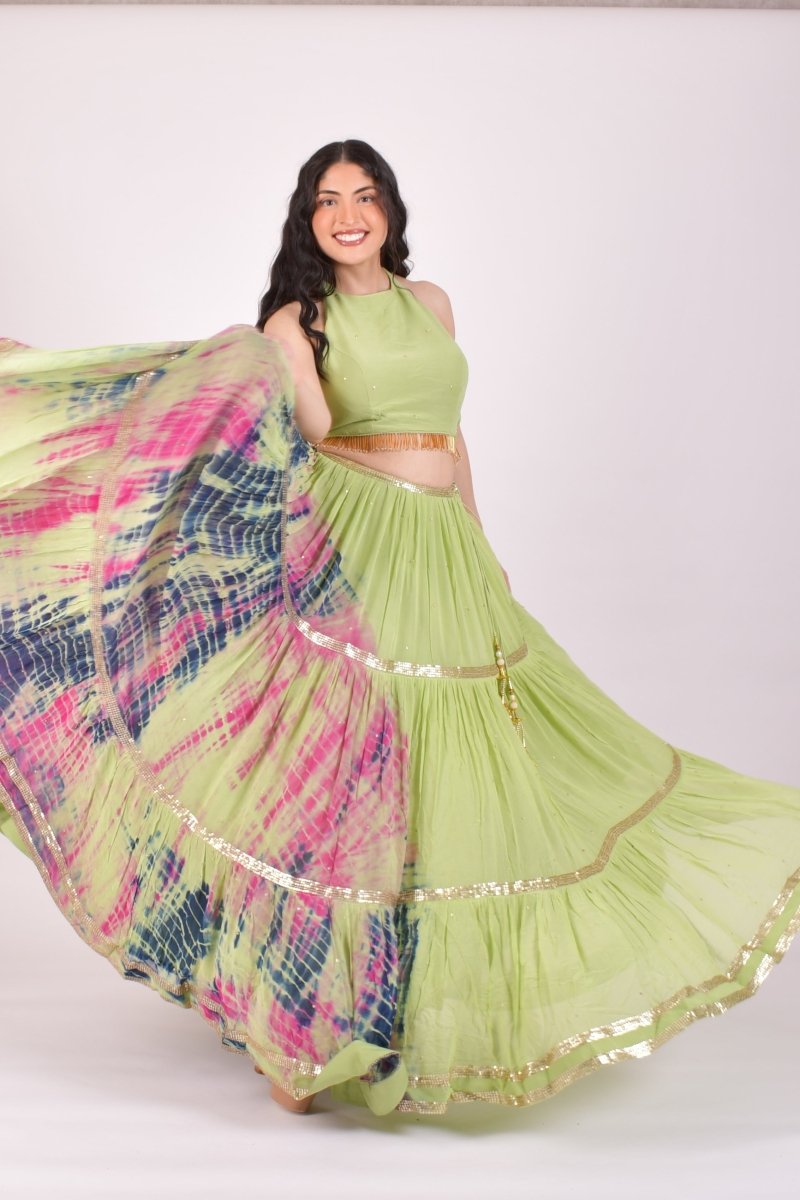A woman modeling a light green traditional outfit with a flared skirt and a multicolored patterned dupatta, posed against a plain light background.