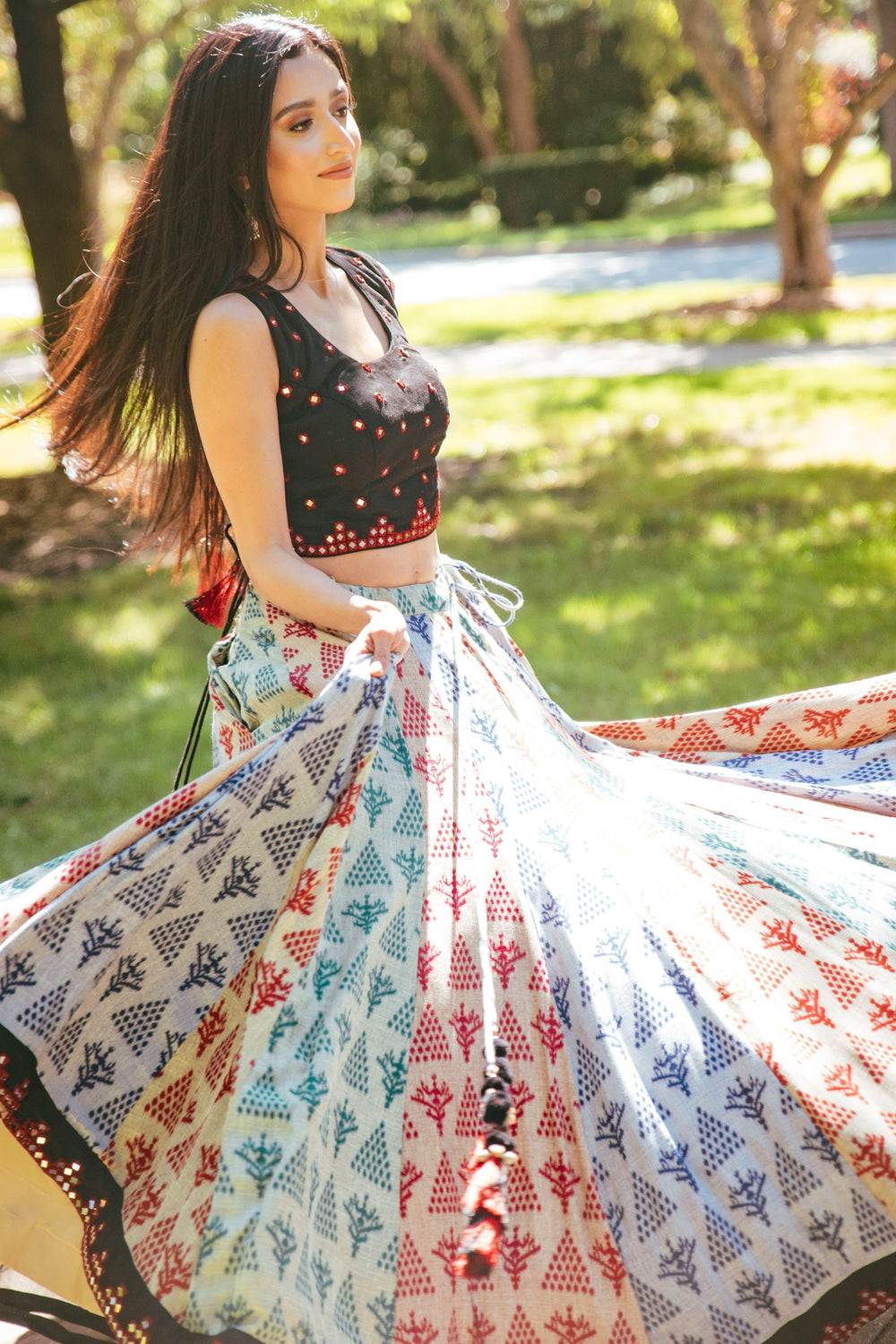 Woman in a black mirror-work cotton choli and a full-flare, hand-block printed lehenga, dramatically twirling outdoors.