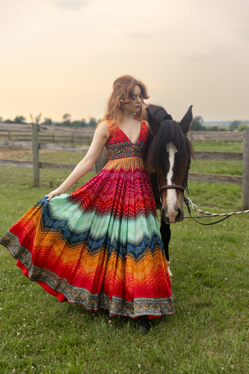 Silk Leandra Long Dress with embroidered top and vibrant bandhani print, worn by a woman next to a horse.