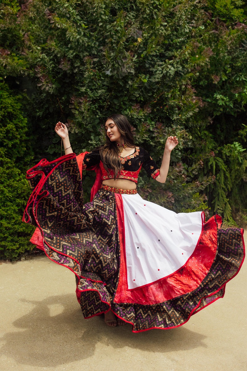 Woman in a dramatic twirling multi-color layered chaniya choli with red, white, black, and gold patterns.