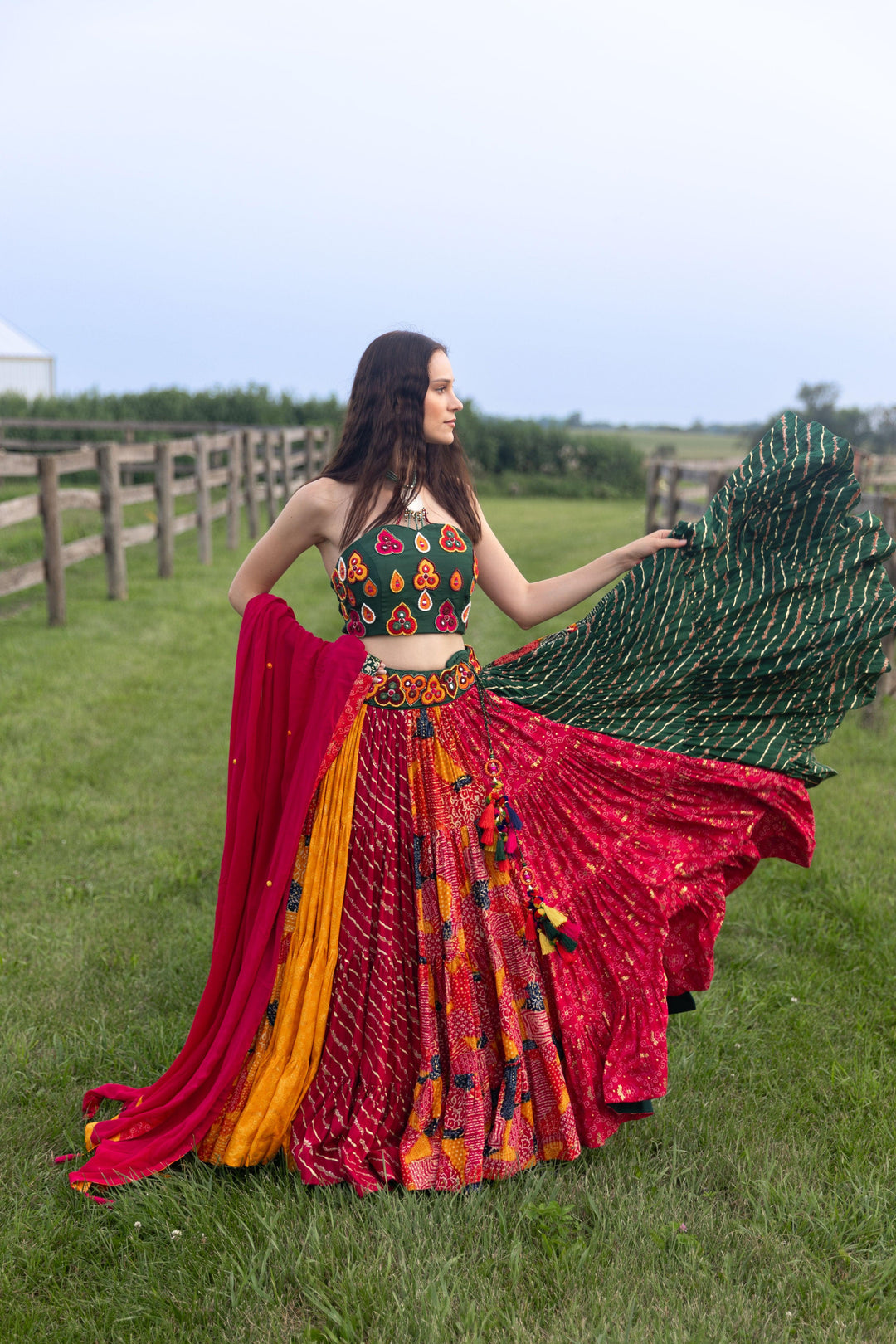 Model in a multi-color, full-flare Chaniya Choli set with a green embroidered necklace top, twirling.