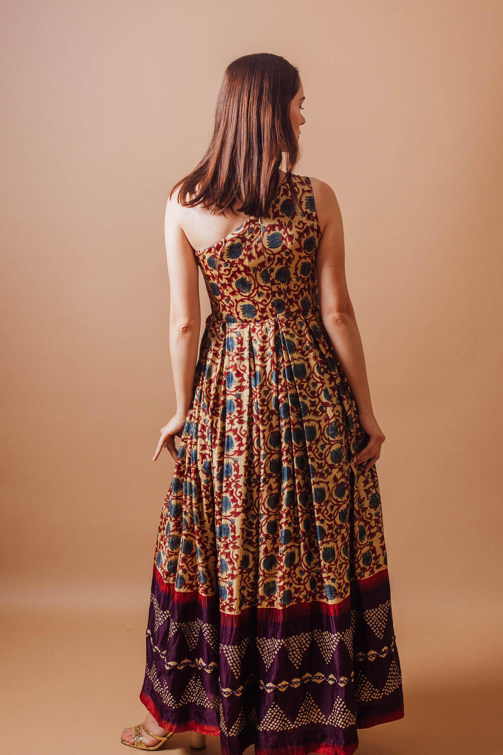 Woman in a flowy Gaji silk one-shoulder dress with all-over ajrakh print and contrasting hem.