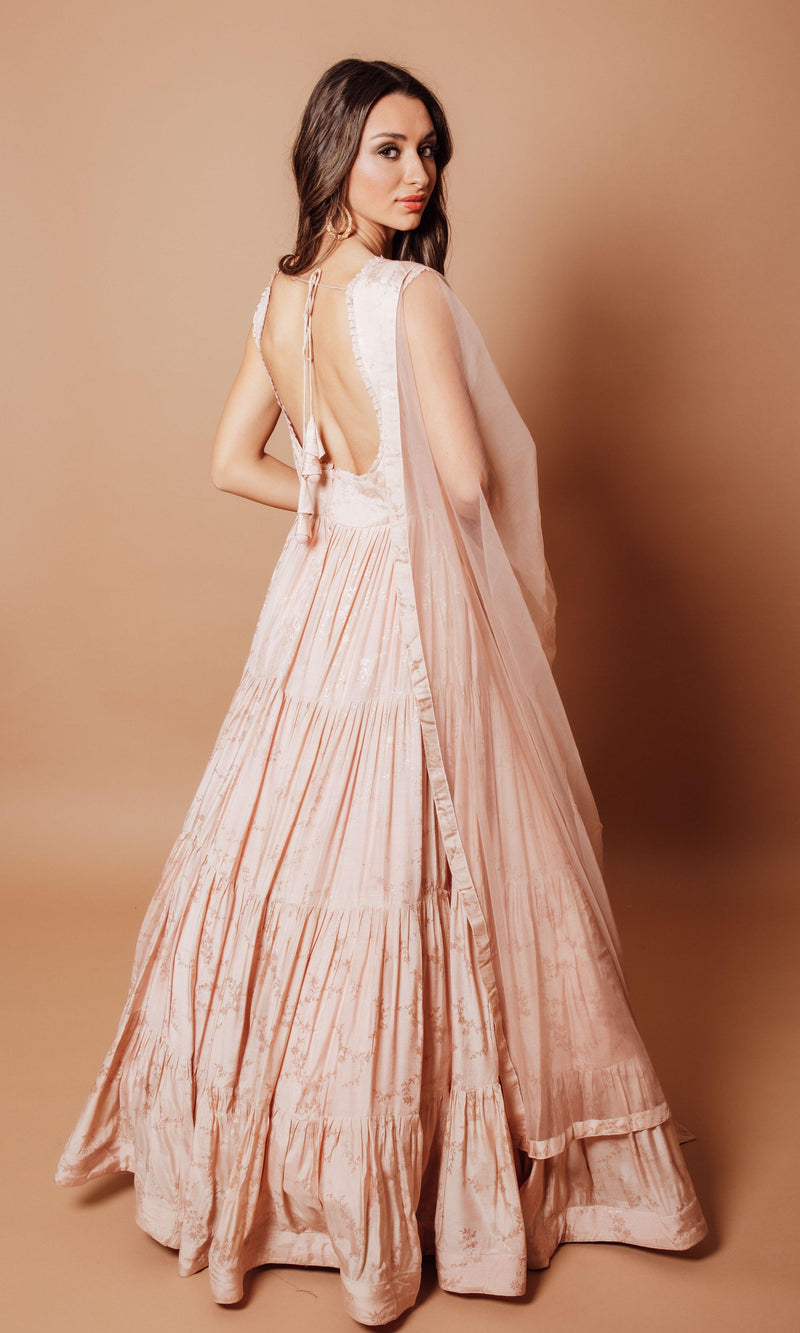 Model in a blush pink jacquard silk tiered dress with self-woven floral pattern, open back, and sheer dupatta.