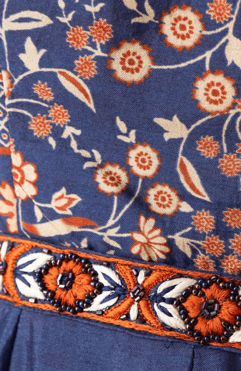 Close-up of a blue silk midi dress with traditional floral print and an embroidered, beaded belt.