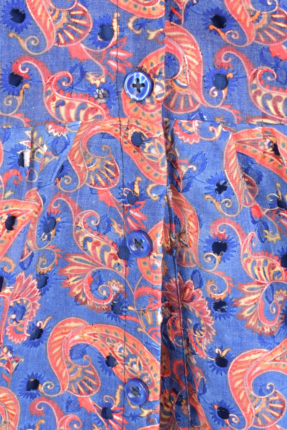 Close-up of a purple Hakoba cotton midi dress with paisley print, eyelet embroidery, and blue buttons.