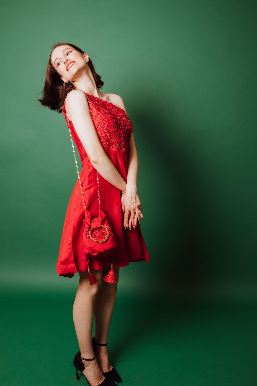 Raw silk red one-shoulder short dress with hand-embroidered torso, paired with a matching red purse.