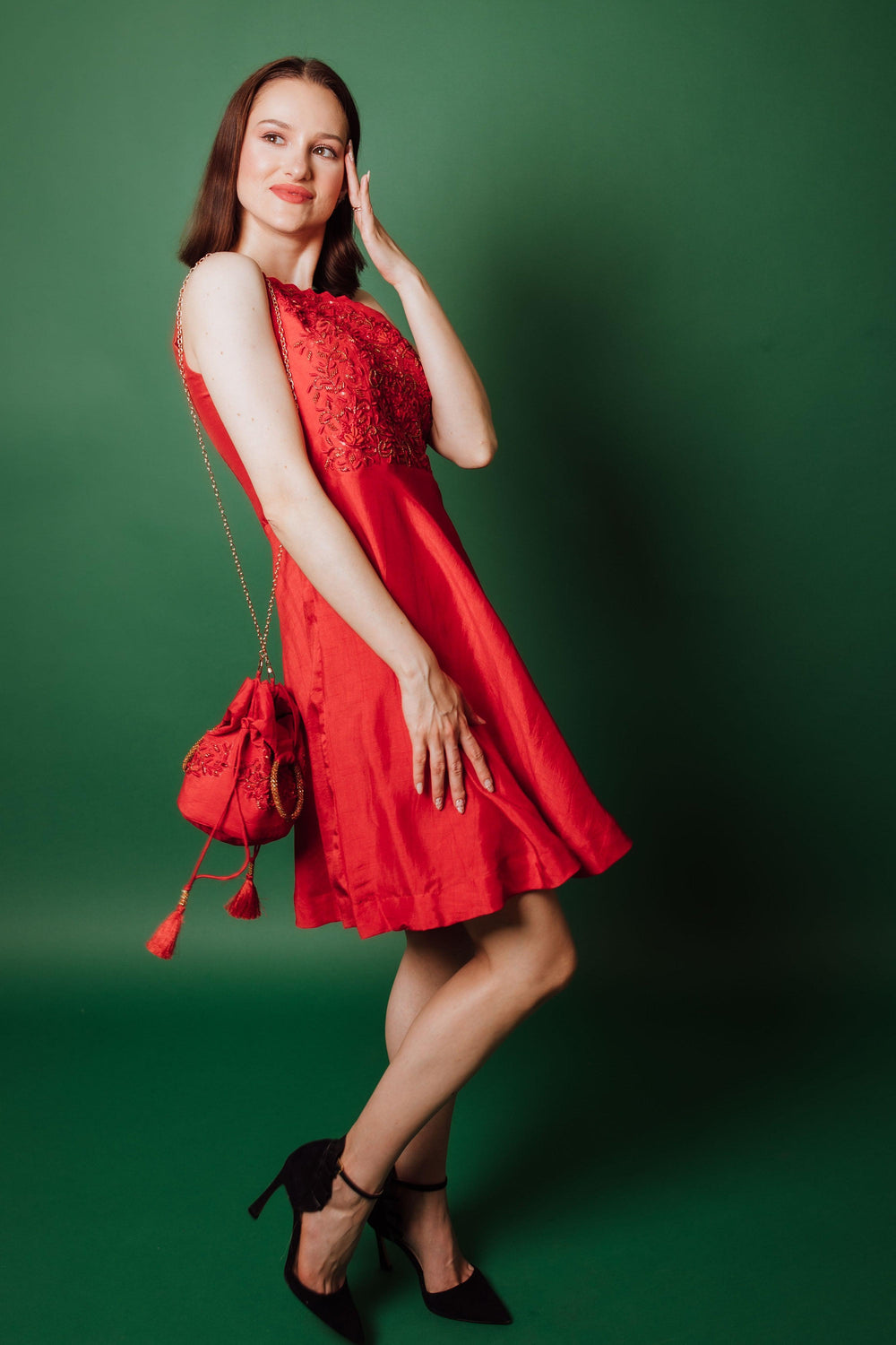 Red raw silk one-shoulder short dress with hand embroidery, paired with a matching drawstring bag.