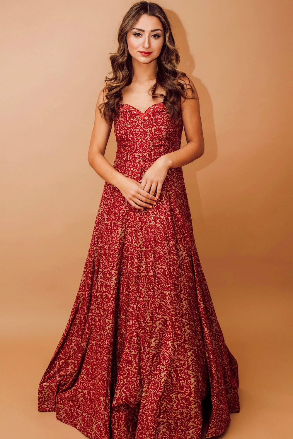 Woman in a red cotton-silk off-shoulder gown with intricate embroidery and an all-over patterned design.