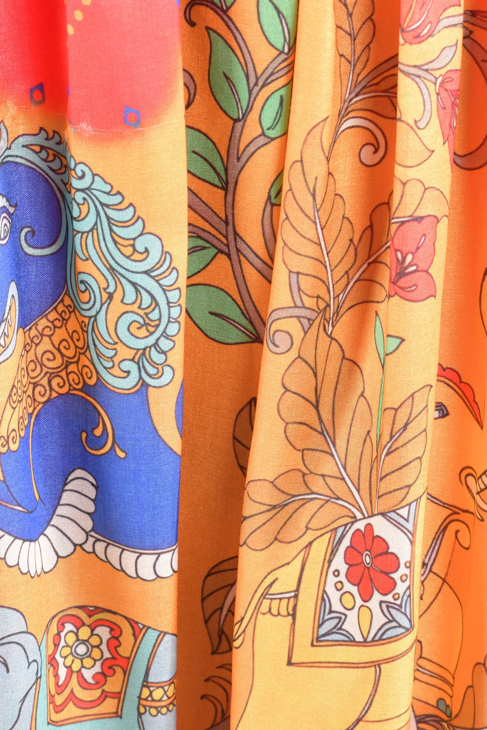 Close-up of a vibrant orange silk midi dress with blue elephant and floral motifs.