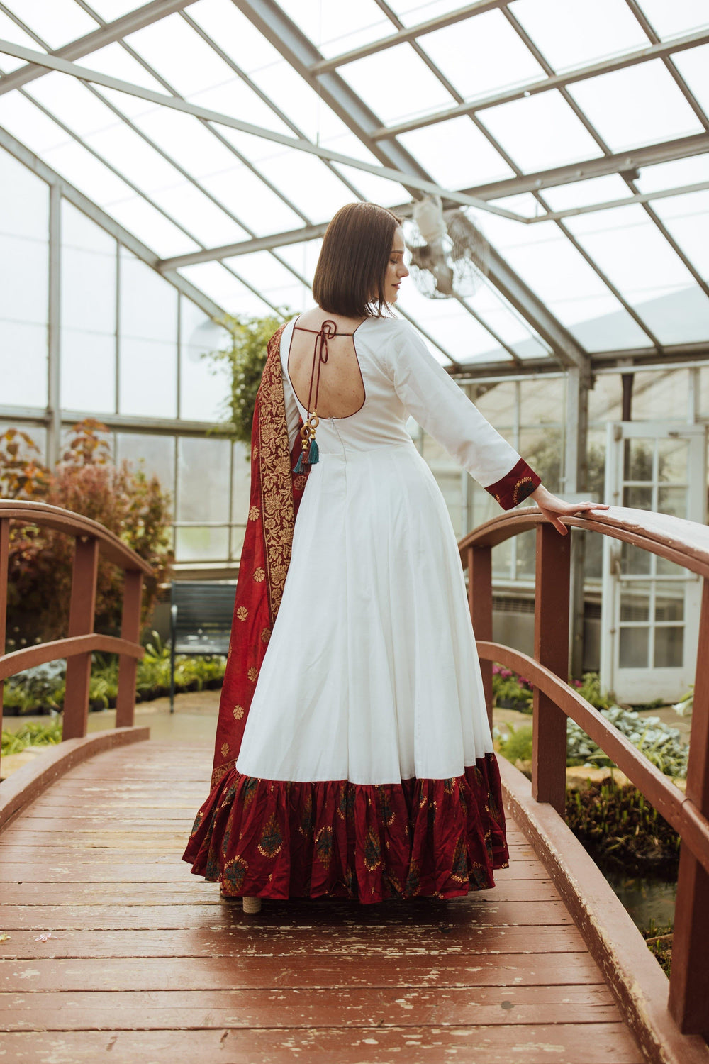 White silk long dress with red embroidery, paired with a crimson Banarasi silk drape, on a wooden bridge.