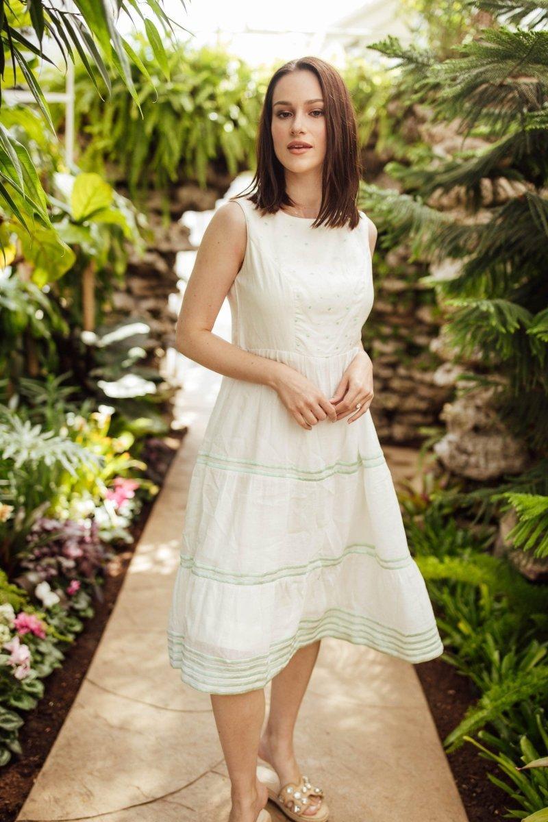 White midi dress with sleeveless design, tiered skirt, and subtle green hand embroidery.