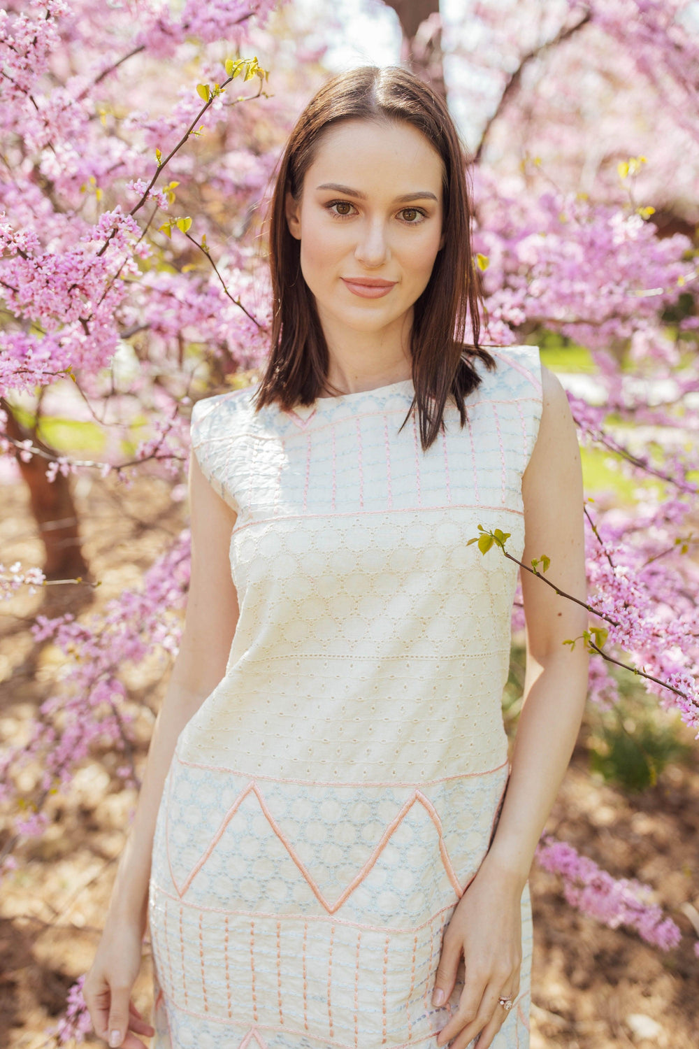White mini dress with geometric coral and ivory eyelet embroidery, sleeveless, cotton fabric.