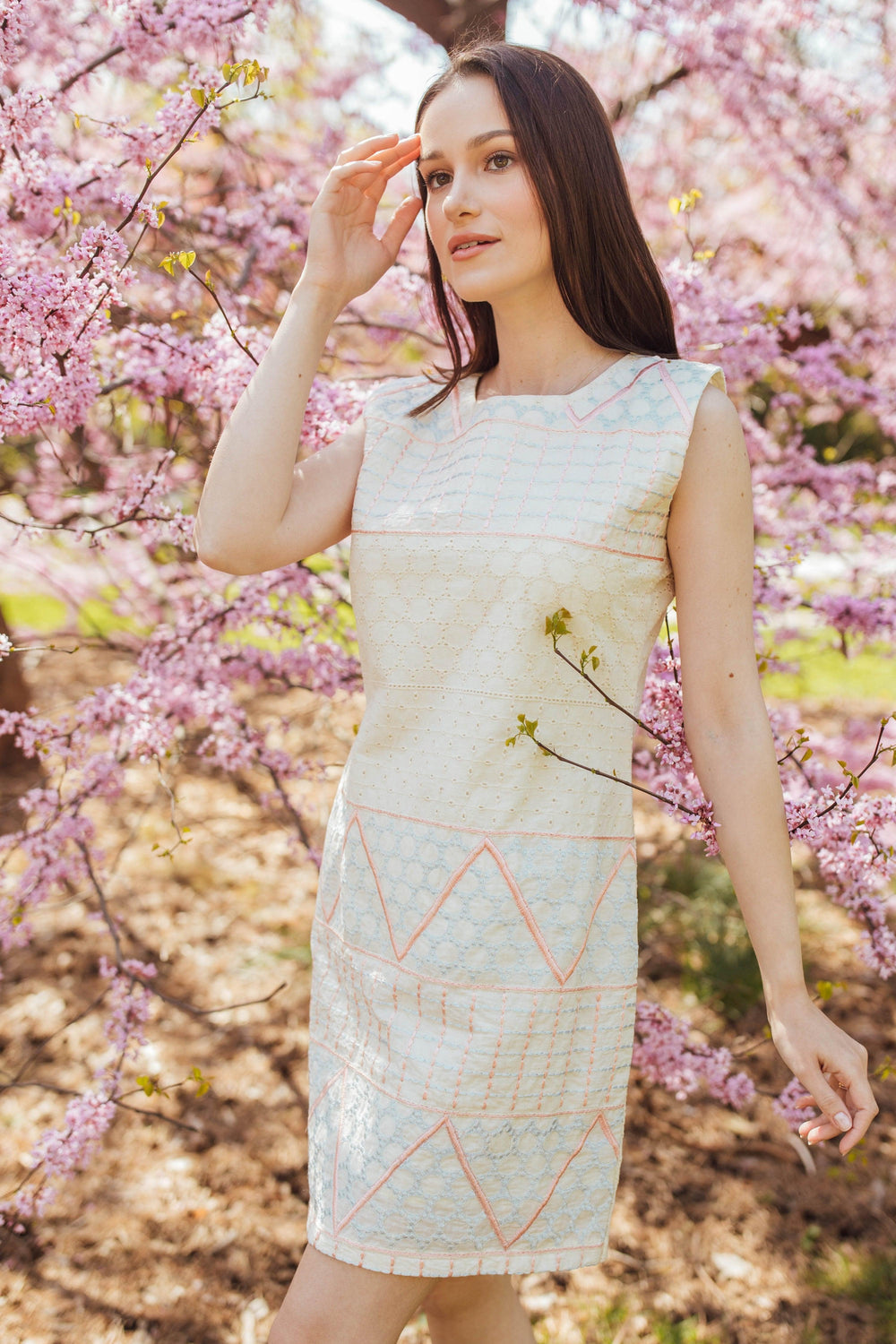 White cotton mini dress with geometric coral and ivory eyelet embroidery, worn by a model.