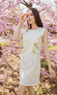 White cotton mini dress with geometric coral and ivory eyelet embroidery, worn by a model.